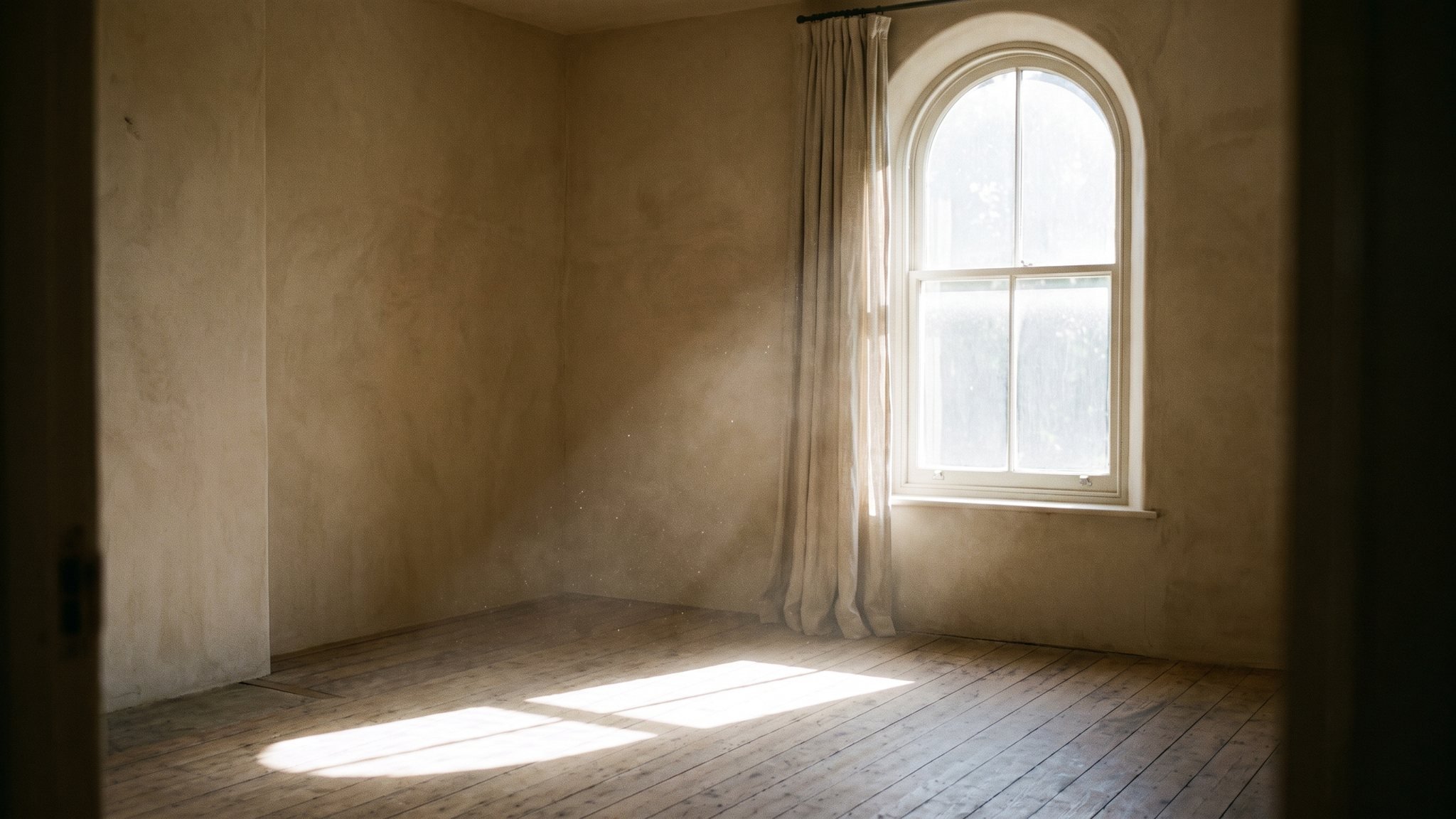 Helles Morgenlicht fällt durch ein hohes Fenster in einen ruhigen sandfarbenen Raum, scharfe Lichtflächen auf dem Holzboden, Staub im Lichtstrahl