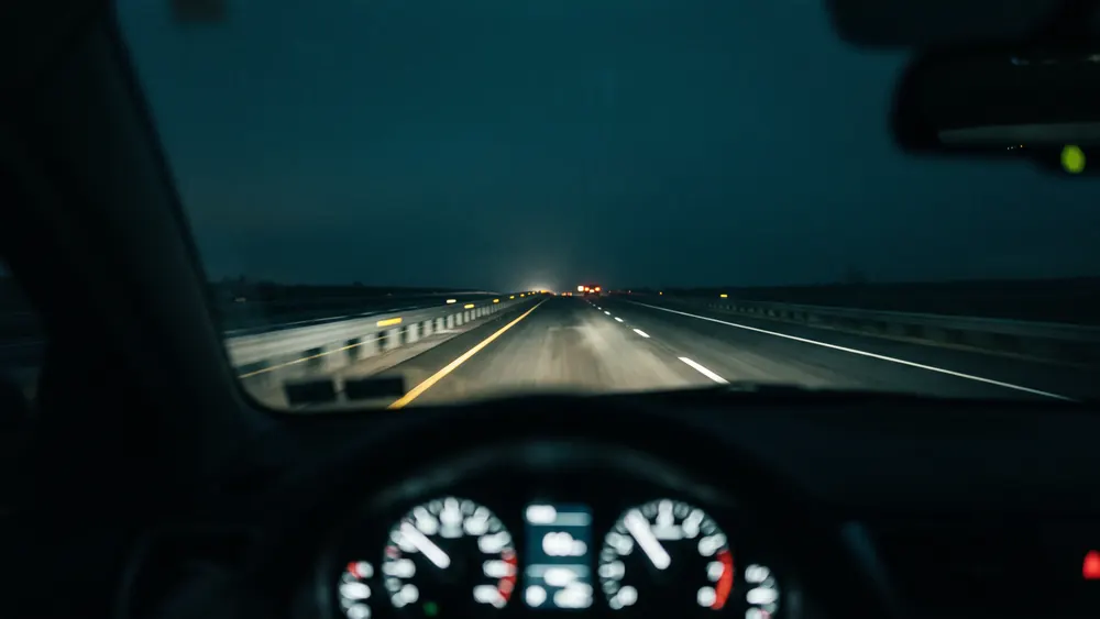 Blick aus der Fahrerperspektive bei Nacht auf eine leere Autobahn, Scheinwerferlicht und reflektierende Fahrbahnmarkierungen ziehen vorbei