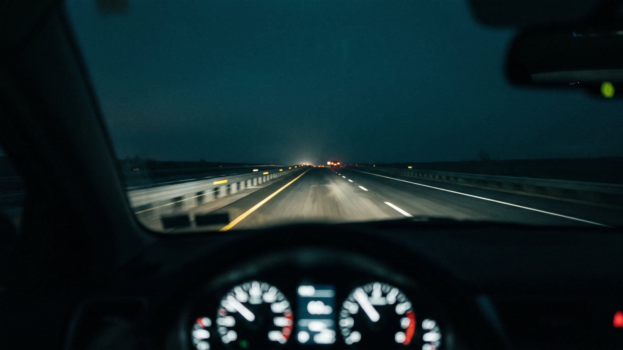 Blick aus der Fahrerperspektive bei Nacht auf eine leere Autobahn, Scheinwerferlicht und reflektierende Fahrbahnmarkierungen ziehen vorbei
